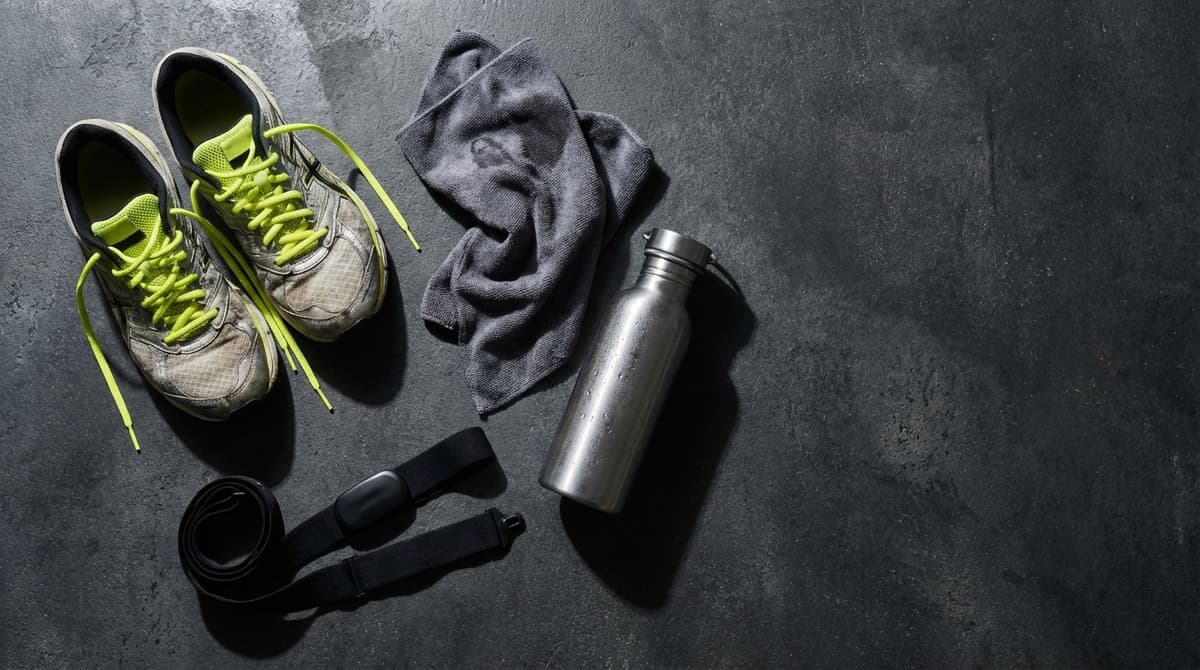 Runner checking heart rate on GPS watch while pausing on a forest trail at golden hour