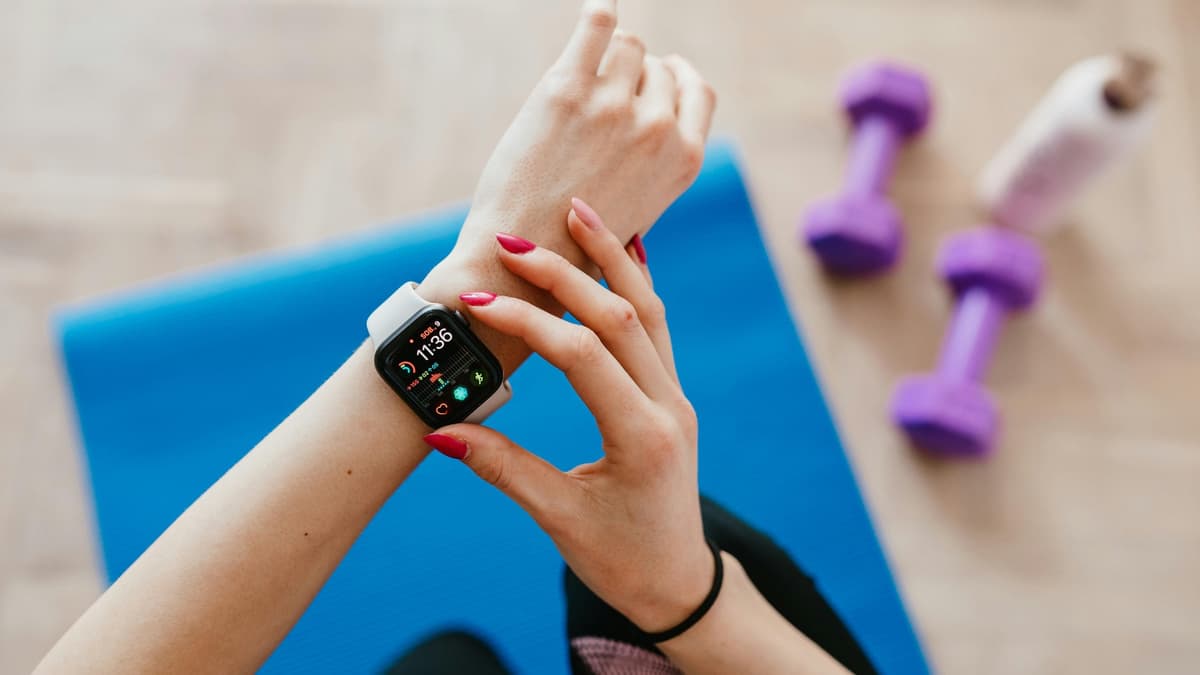 Multiple wearable devices including a smartwatch and ring tracker laid out on a minimalist desk next to a laptop